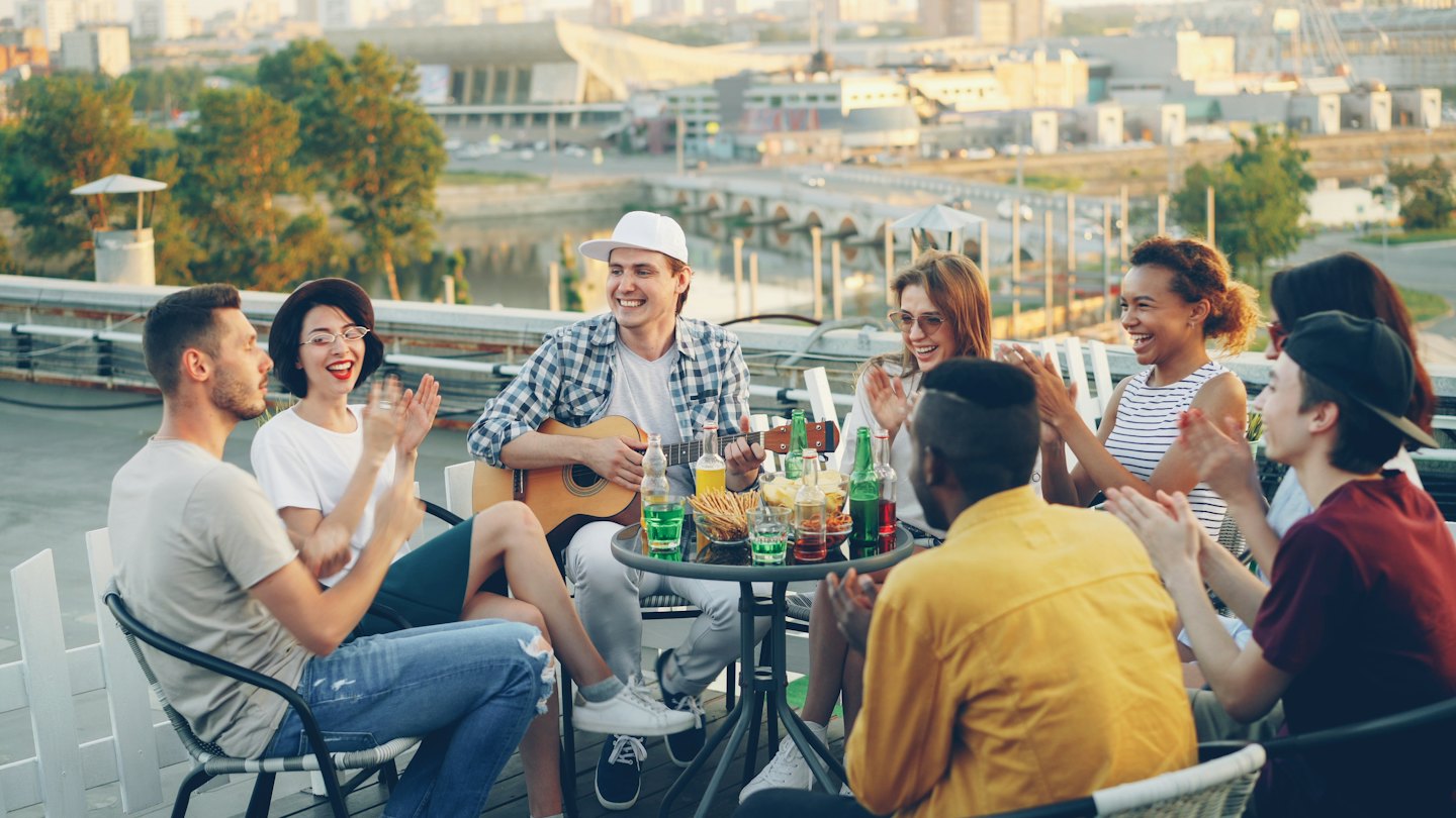 Giovani adulti socializzano e ridono a una festa sul tetto con musica.